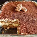 A delicious Biscoff Tiramisu in a glass dish, topped with cocoa powder and two Biscoff cookies.