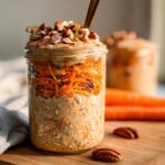 A close-up of Carrot Cake Overnight Oats in a mason jar, topped with shredded carrots and nuts.