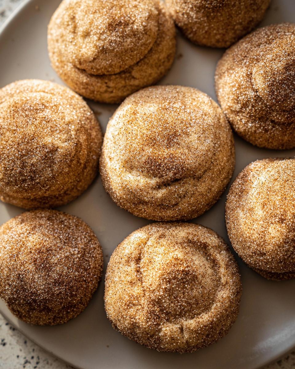 A close-up of several chewy churro cookies, generously coated in cinnamon sugar, arranged on a grey plate.