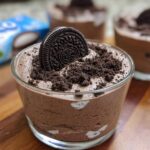 A close-up of a glass of 3-ingredient Cookies and Cream Mousse, topped with crushed Oreos and a whole Oreo cookie.