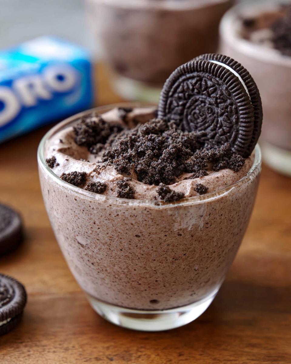 A close-up of a glass of creamy Cookies and Cream Mousse, topped with crushed Oreos and a whole Oreo cookie.