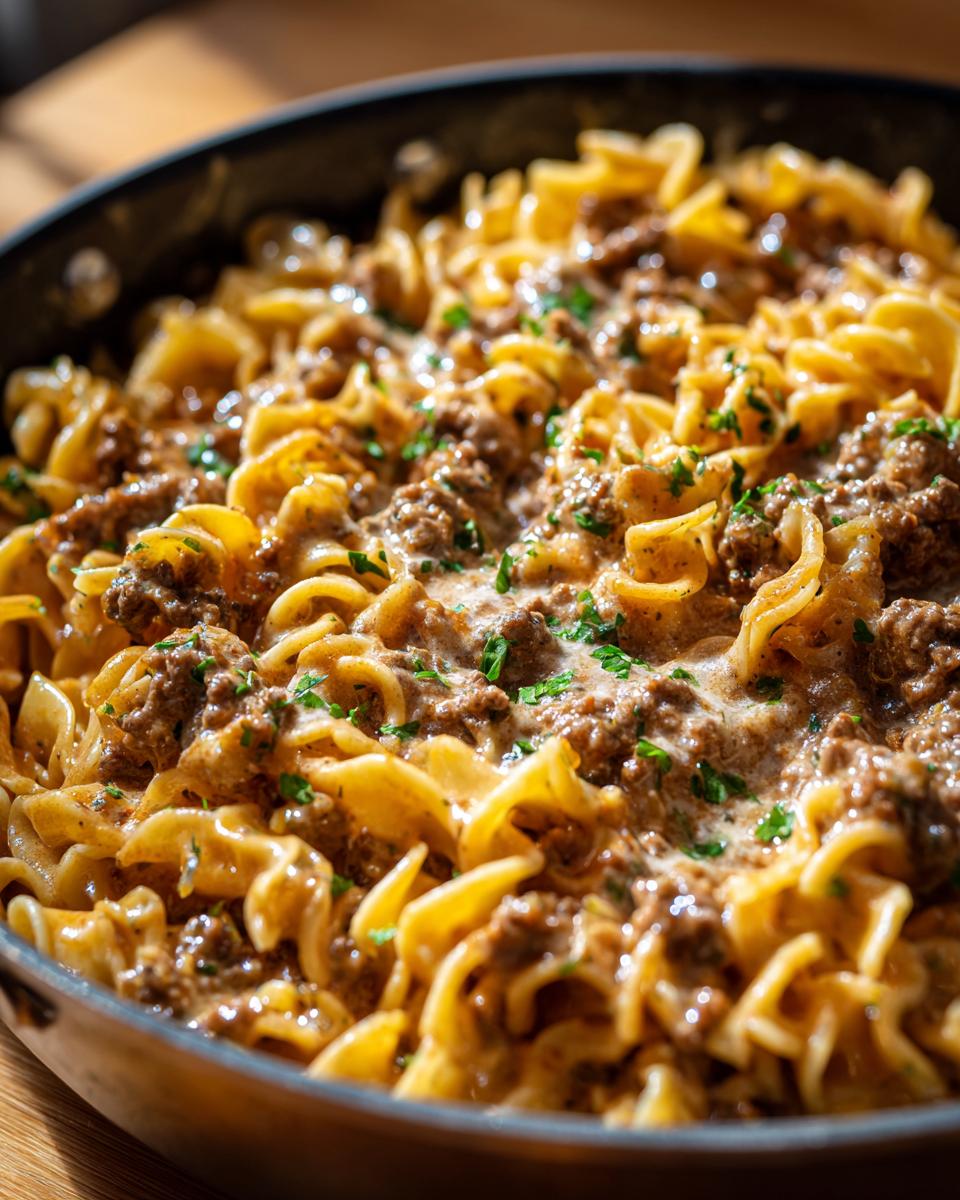 Close-up of a creamy beef stroganoff skillet meal with ground beef and pasta, garnished with parsley.