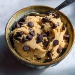 A bowl of delicious protein cookie dough loaded with chocolate chips, ready to be eaten with a spoon.