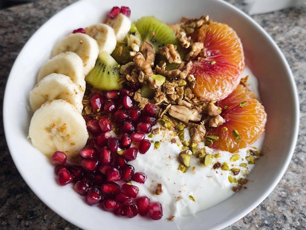 A vibrant and delicious Easy Yogurt Granola Bowl topped with banana, kiwi, orange slices, pomegranate seeds, and granola.