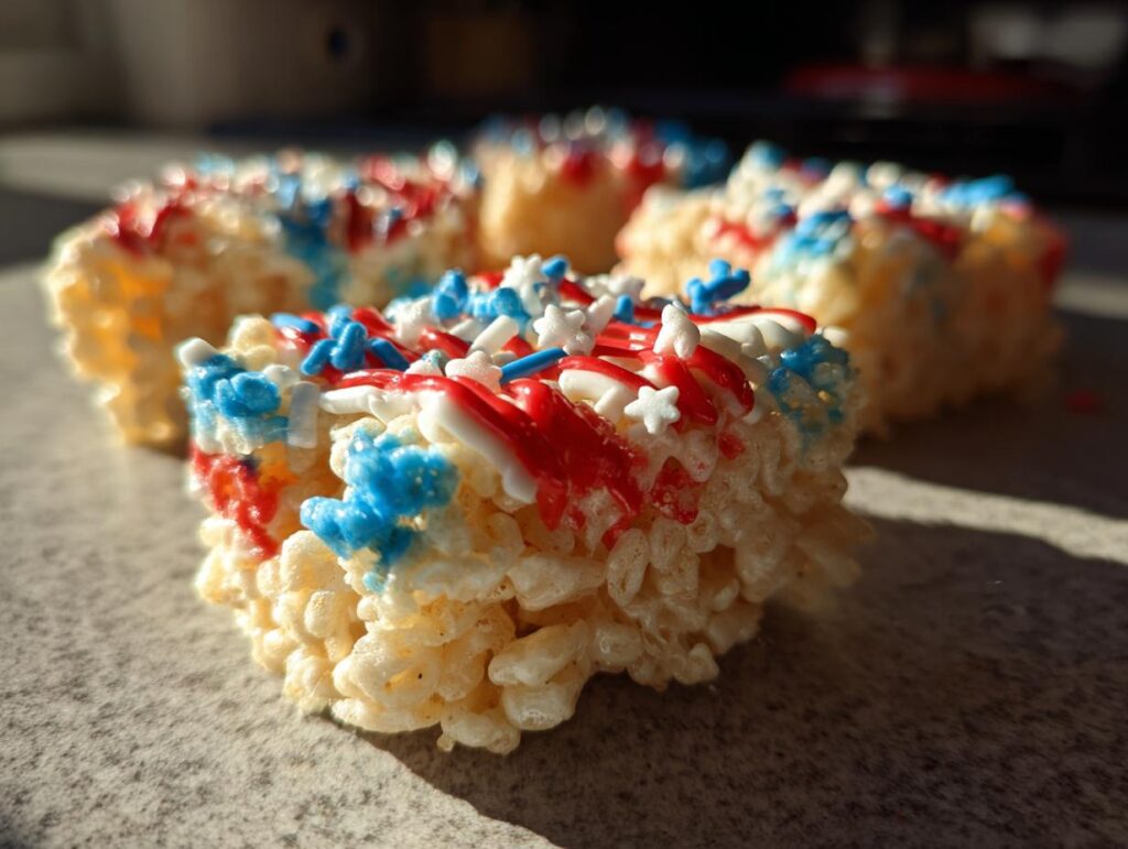 Close-up of Firecracker Rice Krispie Treats decorated with red, white, and blue icing and sprinkles for Fourth of July.