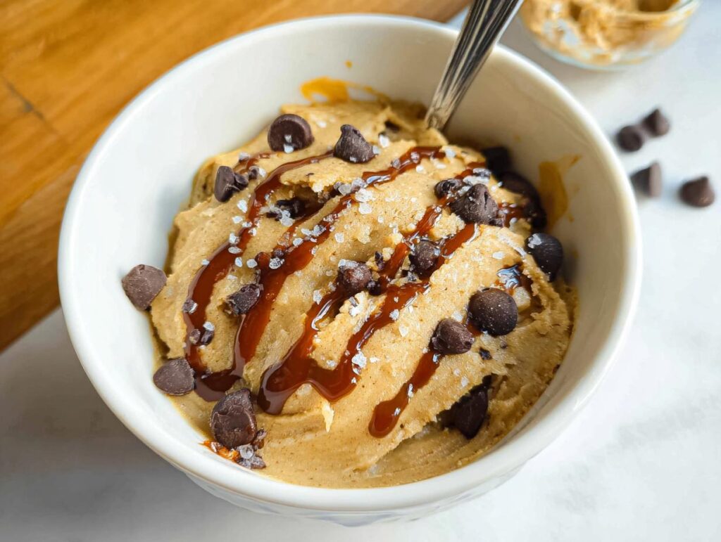 A bowl of creamy Greek Yogurt Cookie Dough topped with chocolate chips, caramel drizzle, and sea salt.