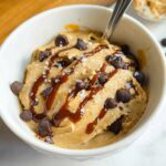 A bowl of creamy Greek Yogurt Cookie Dough topped with chocolate chips, caramel drizzle, and sea salt.