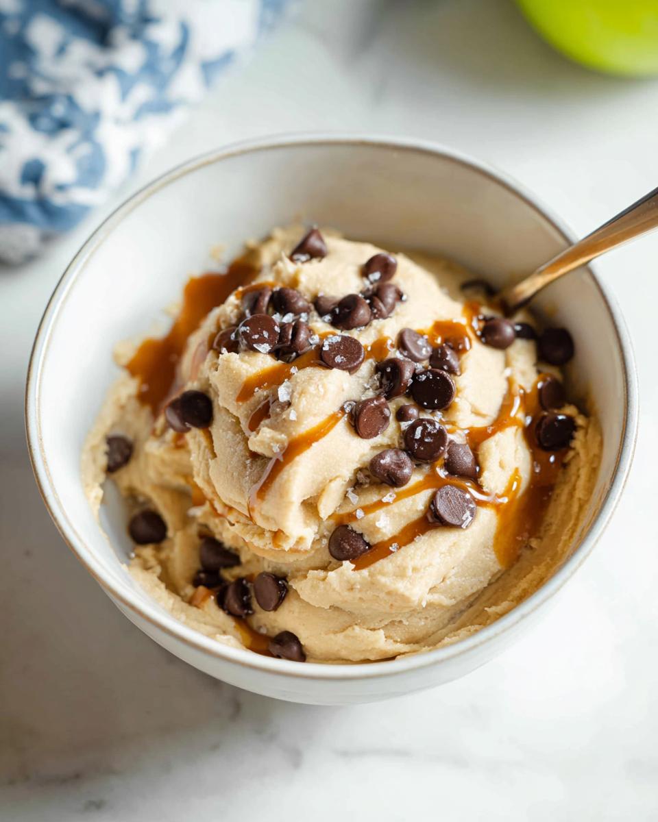 A bowl of Greek Yogurt Cookie Dough topped with chocolate chips, caramel drizzle, and sea salt.