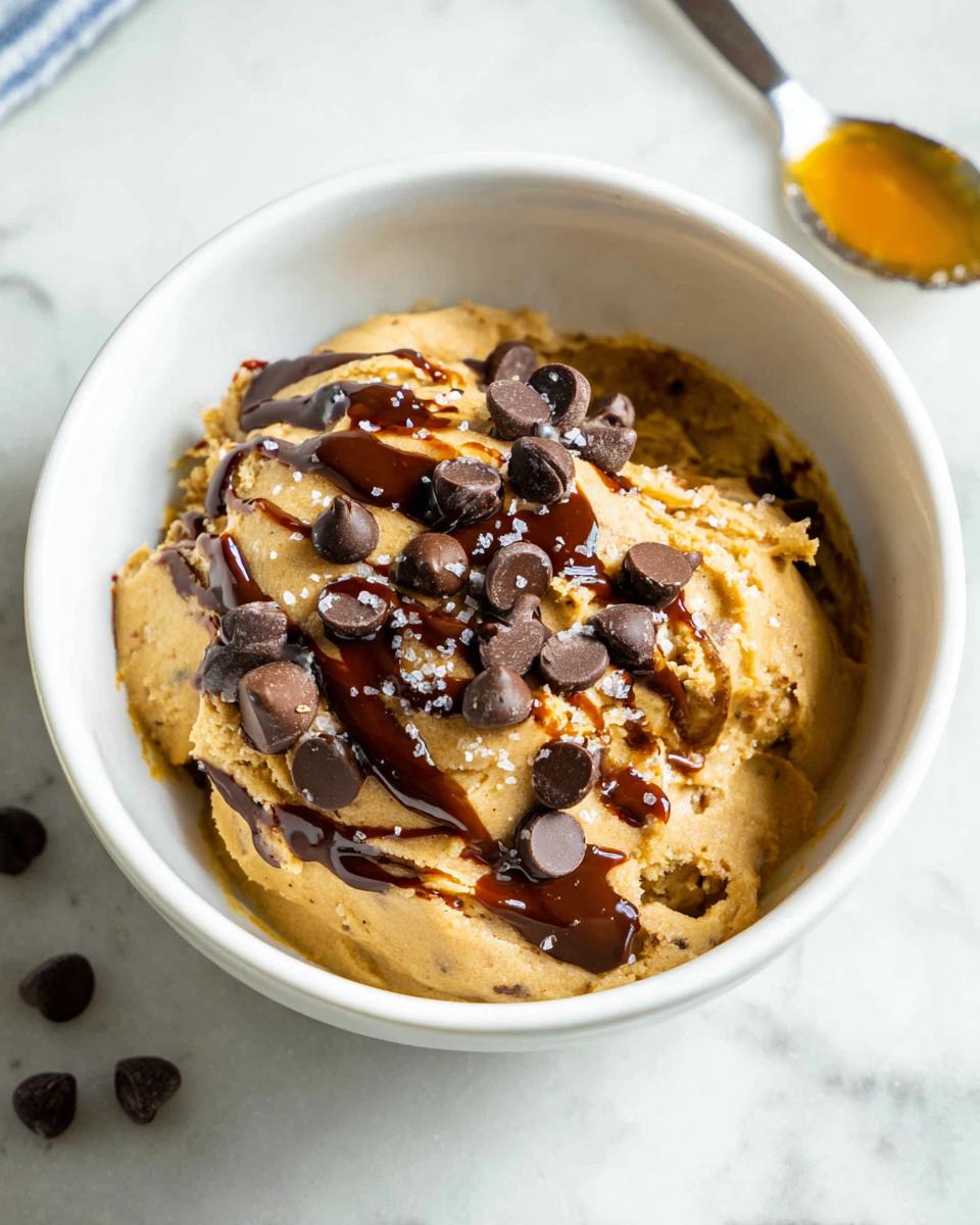 A bowl of delicious Greek Yogurt Cookie Dough topped with chocolate chips, chocolate syrup, and sea salt.
