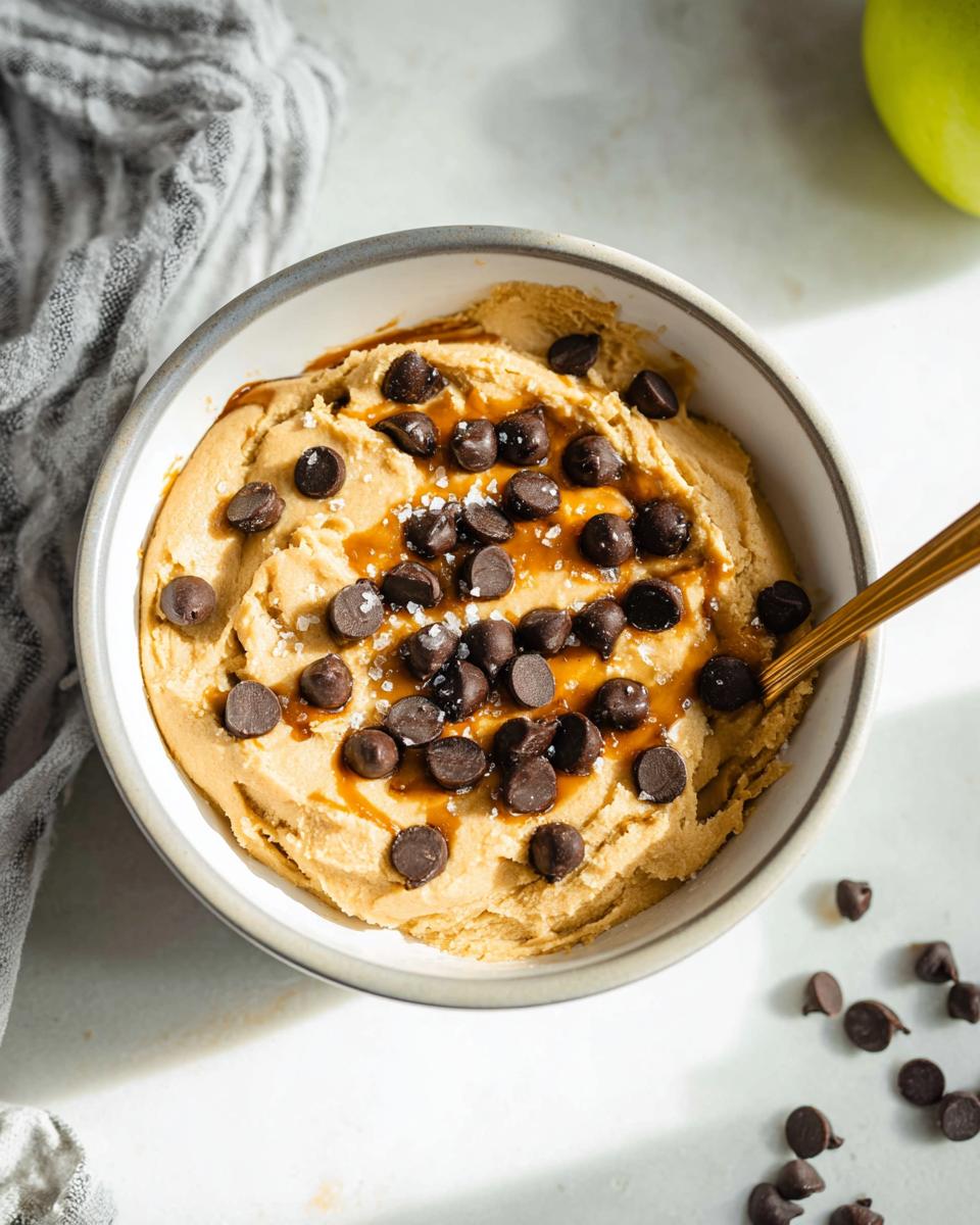 A bowl of Greek Yogurt Cookie Dough topped with chocolate chips and caramel drizzle, sprinkled with sea salt.