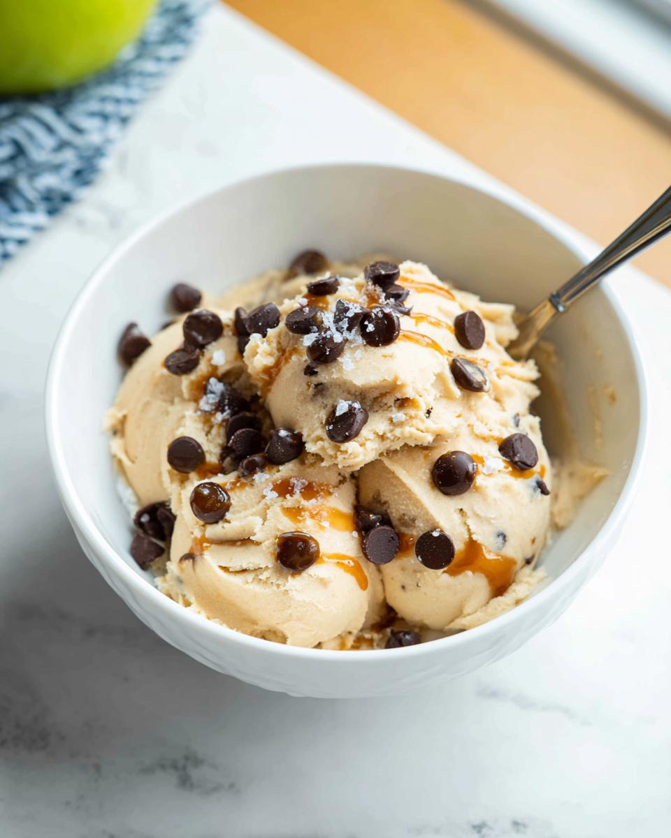 A bowl of creamy Greek Yogurt Cookie Dough ice cream topped with chocolate chips and caramel drizzle.