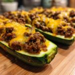 Close-up of baked zucchini boats filled with seasoned ground beef and topped with melted cheddar cheese.
