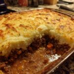 A close-up of a rich and hearty Shepherd's Pie, featuring a layer of seasoned ground beef and vegetables topped with golden-brown mashed potatoes.
