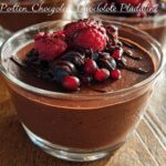 A close-up of a glass ramekin filled with rich High Protein Chocolate Pudding, topped with fresh raspberries, blueberries, and a drizzle of chocolate sauce.