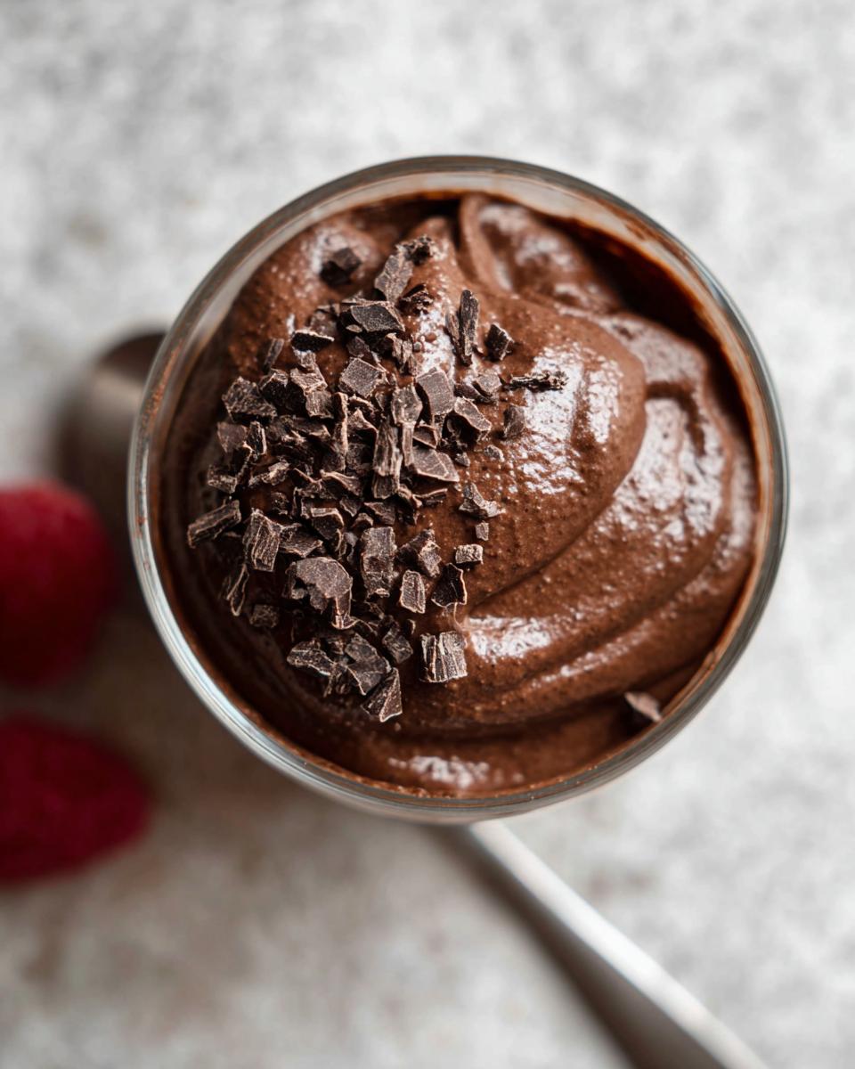 A close-up overhead view of a glass of rich High Protein Chocolate Pudding topped with dark chocolate shavings.
