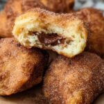 Close-up of homemade churro bites coated in cinnamon sugar, with one bite broken open to reveal a gooey Nutella filling.