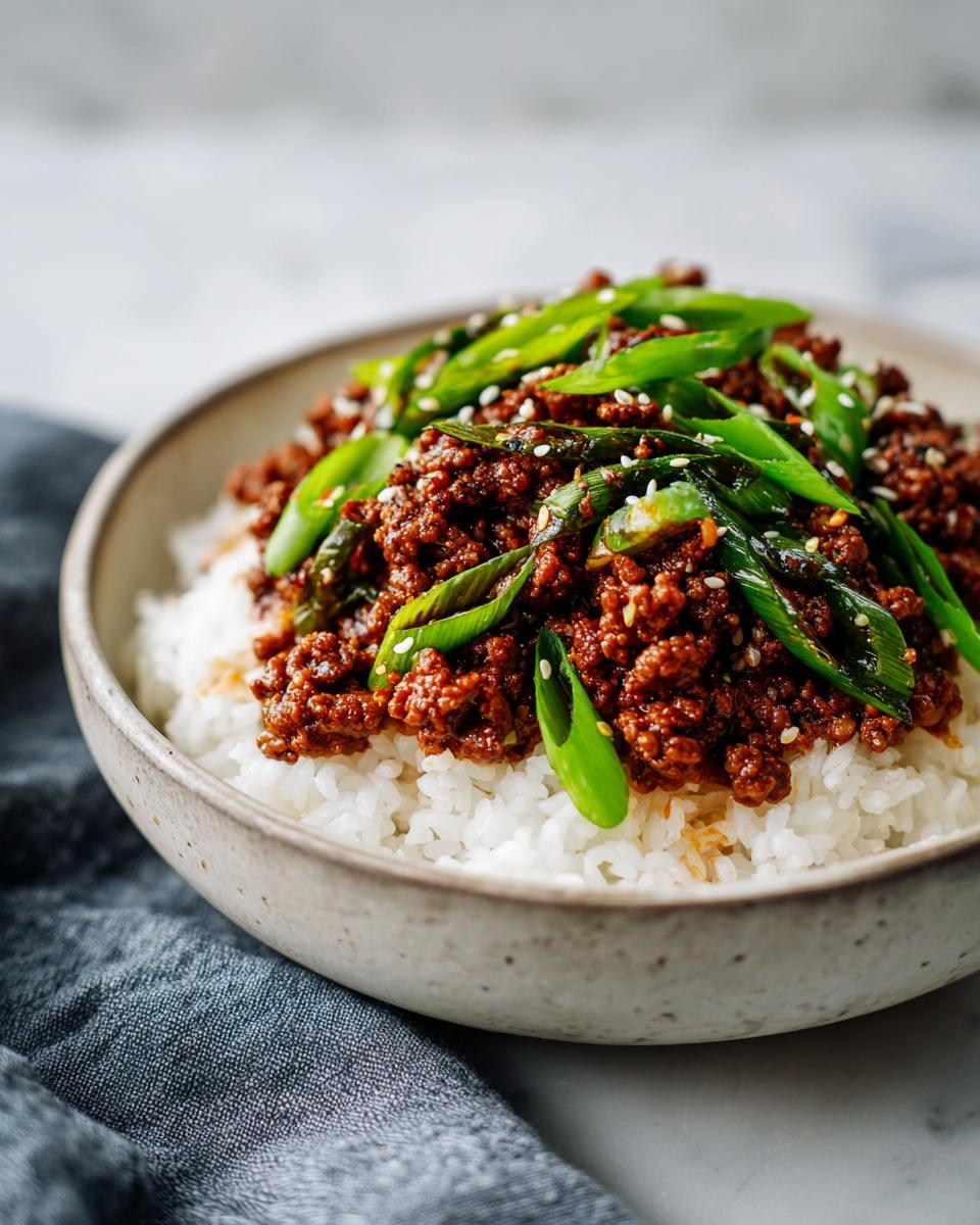 A close-up of a Korean beef rice bowl topped with ground beef, green onions, and sesame seeds.