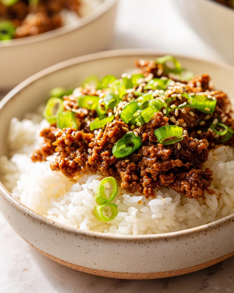 A close-up of a Korean beef rice bowl topped with ground beef, green onions, and sesame seeds.