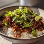 A close-up of a bowl of Korean Beef Rice Bowls, featuring seasoned ground beef over white rice, topped with green onions and sesame seeds.