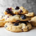 A stack of three Lemon Blueberry Cheesecake Cookies, with the top cookie broken to show the gooey center and blueberries.