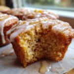 Close-up of a moist peach muffin with a bite taken out, drizzled with vanilla glaze.