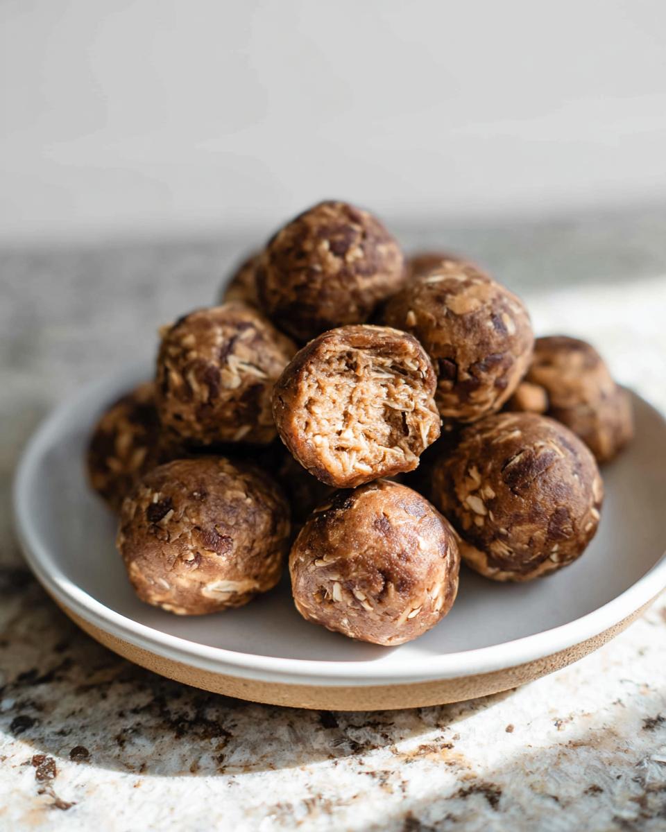 A close-up of No-Bake Chocolate Peanut Butter Protein Balls piled on a plate, with one ball bitten in half.