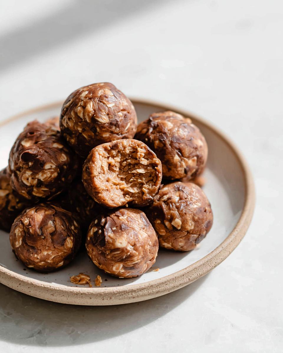 A close-up shot of a stack of No-Bake Chocolate Peanut Butter Protein Balls on a plate, with one ball broken in half.