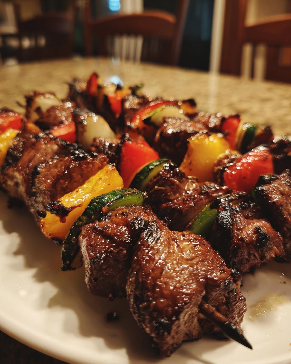 Close-up of grilled steak kabobs with colorful bell peppers and onions, showcasing juicy, charred steak.