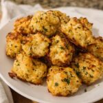 A pile of golden brown Two Ingredient Cottage Cheese Tots sprinkled with fresh parsley on a white plate.