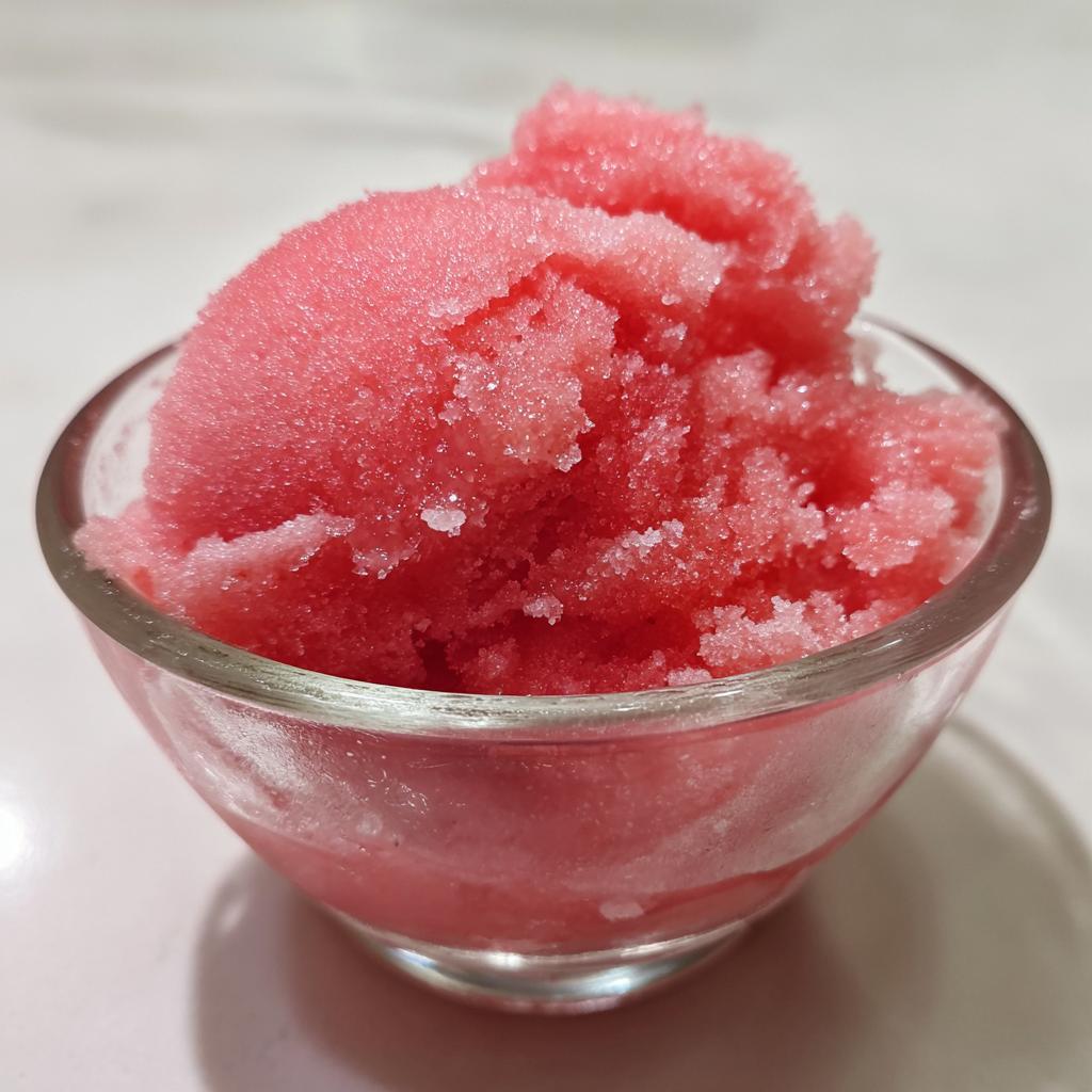 A close-up of a glass bowl filled with vibrant pink watermelon sorbet, showcasing its icy texture.